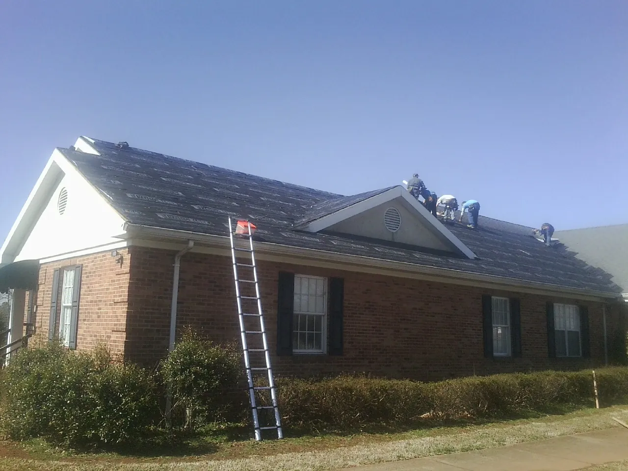 Crew tearing shingles off a brick ranch roof with a ladder set — Metal Roof Repair work by our crew in Columbia